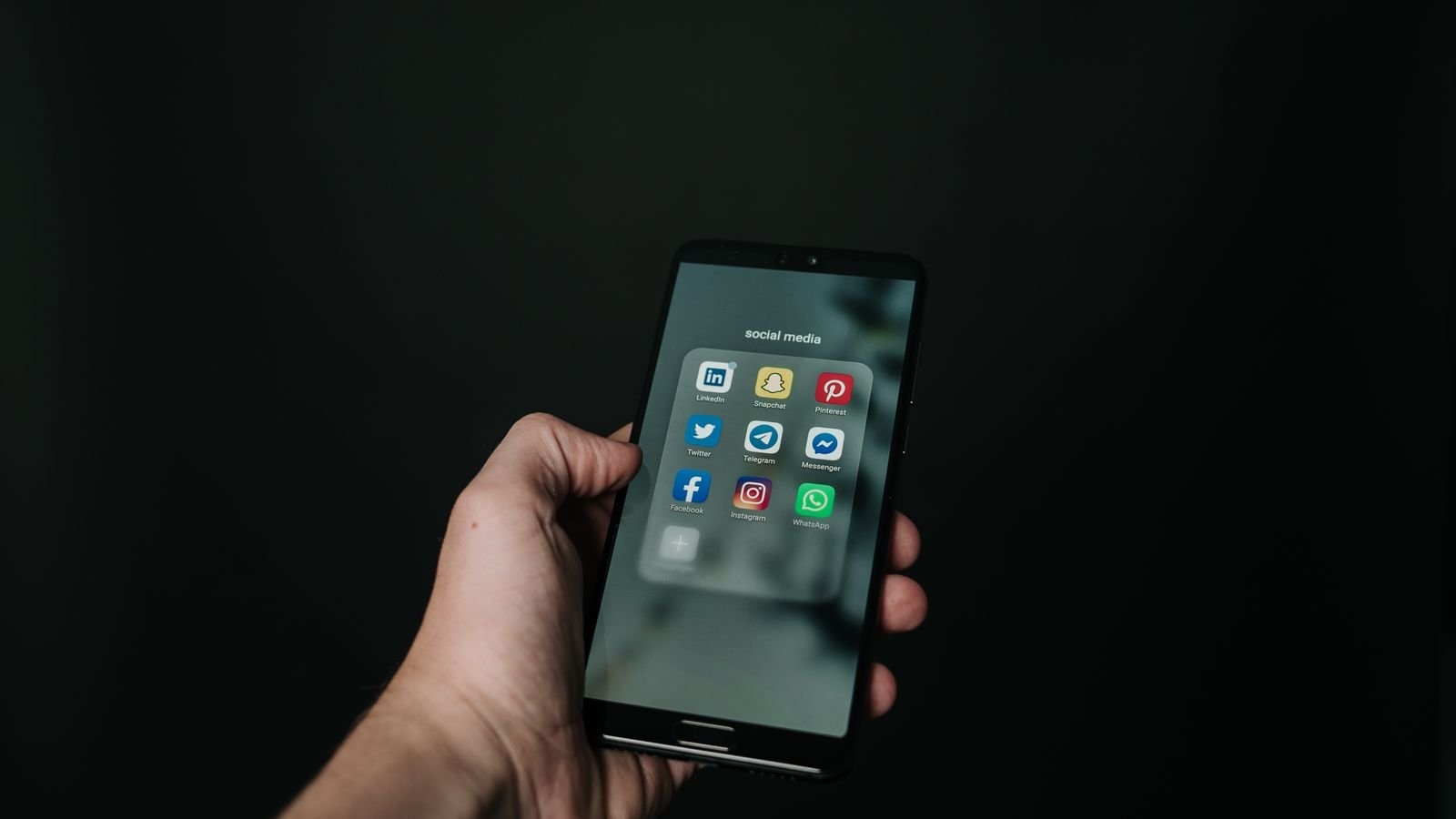 Hand holding a smartphone displaying social media app icons on a dark background